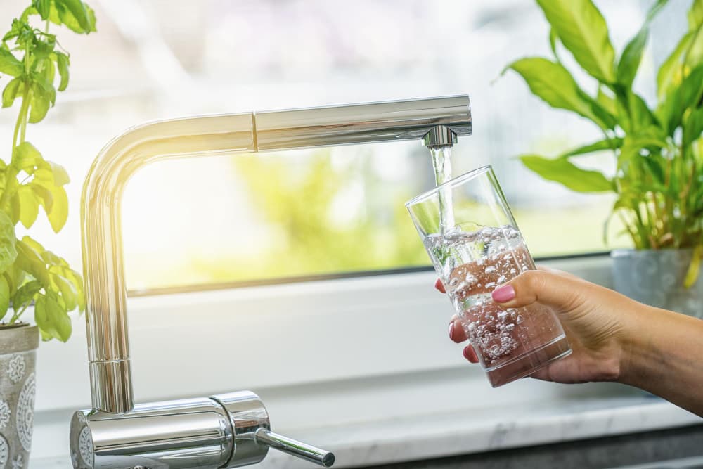 Mujer llenando un vaso de agua del grifo en la cocina