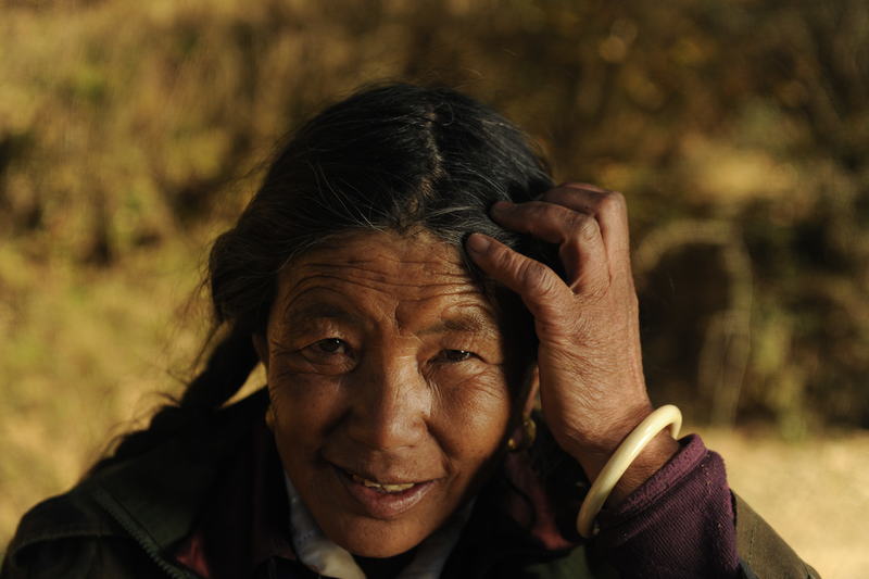 Mujer mayor sonríe mientras se acomoda el cabello, en un entorno rural afectado por el cambio climático.