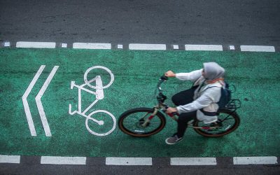 Mujer pedaleando por una ciclovía urbana pintada de verde, con señalización vial de uso exclusivo para bicicletas, en una ciudad.