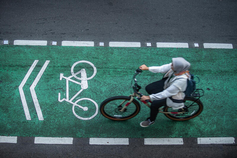 Mujer pedaleando por una ciclovía urbana pintada de verde, con señalización vial de uso exclusivo para bicicletas, en una ciudad.