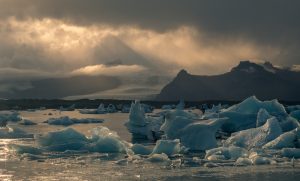 Paisaje ártico con icebergs flotando y cordillera oscura al fondo bajo un cielo nublado, ilustrando el deshielo polar.