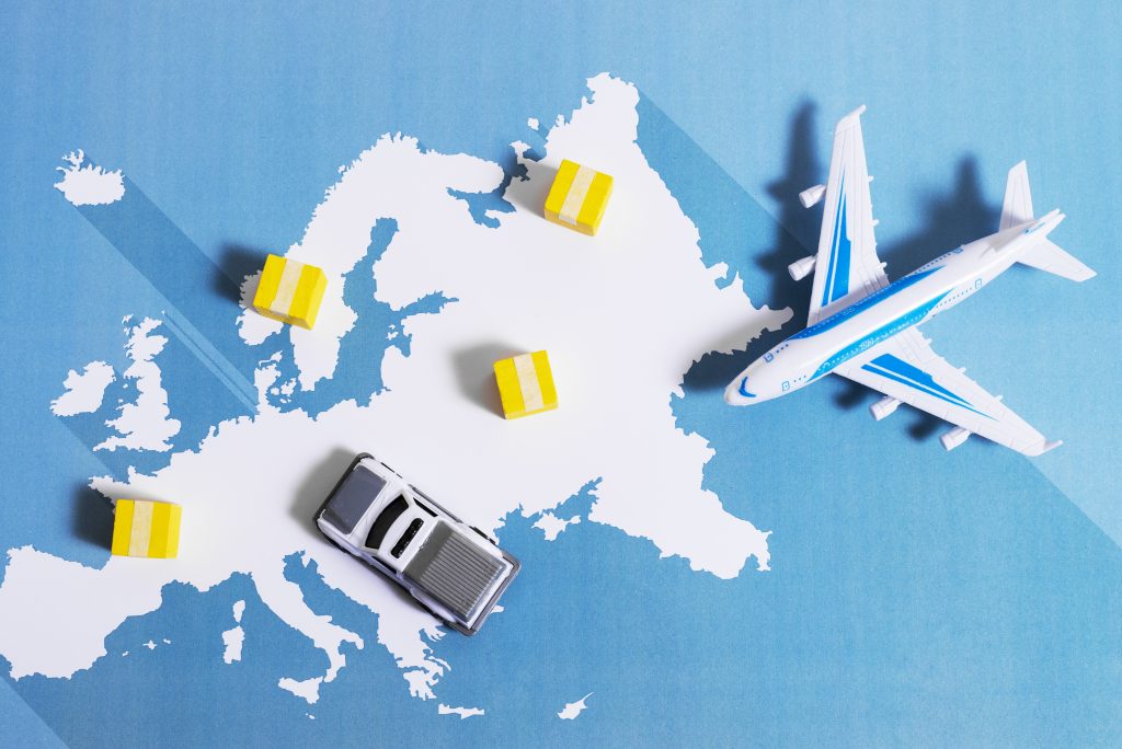 Mapa ilustrado de Europa con miniaturas de un avión, un automóvil y cajas de carga amarilla, representando el comercio y la logística internacional.