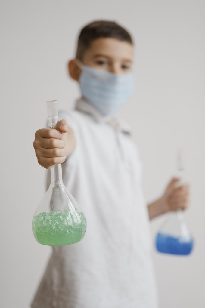 Niño con barbijo sosteniendo matraces con líquidos de colores, representando el vínculo entre ciencia y medio ambiente.