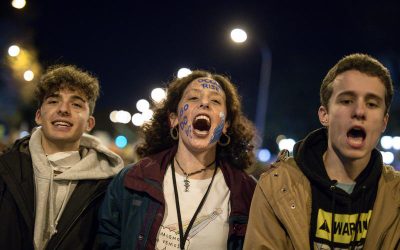 Tres jóvenes manifestantes gritan consignas ambientales durante una protesta nocturna; uno de ellos lleva pintado el rostro con mensajes ecológicos.