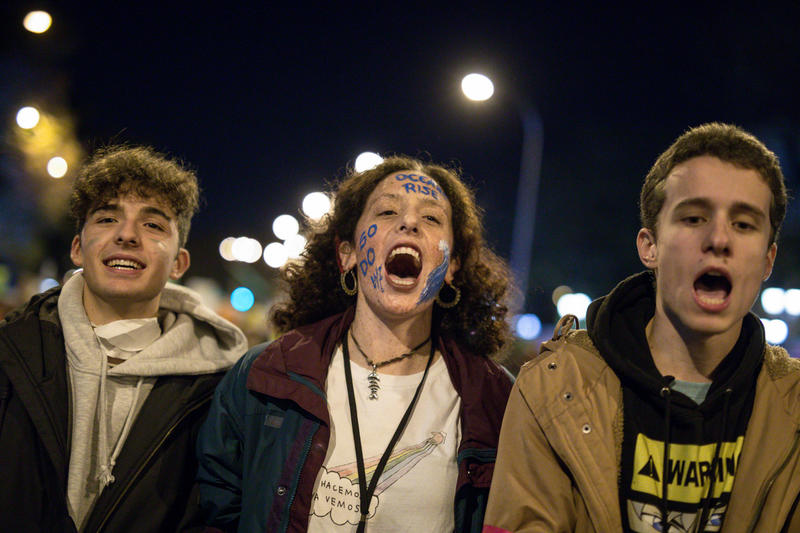 Tres jóvenes manifestantes gritan consignas ambientales durante una protesta nocturna; uno de ellos lleva pintado el rostro con mensajes ecológicos.