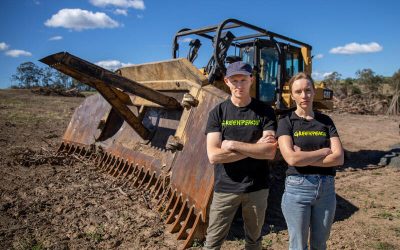 Activistas de Greenpeace con camisetas negras posan frente a una topadora en un terreno desmontado como protesta contra la deforestación en Argentina.