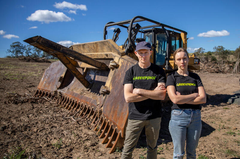 Activistas de Greenpeace con camisetas negras posan frente a una topadora en un terreno desmontado como protesta contra la deforestación en Argentina.