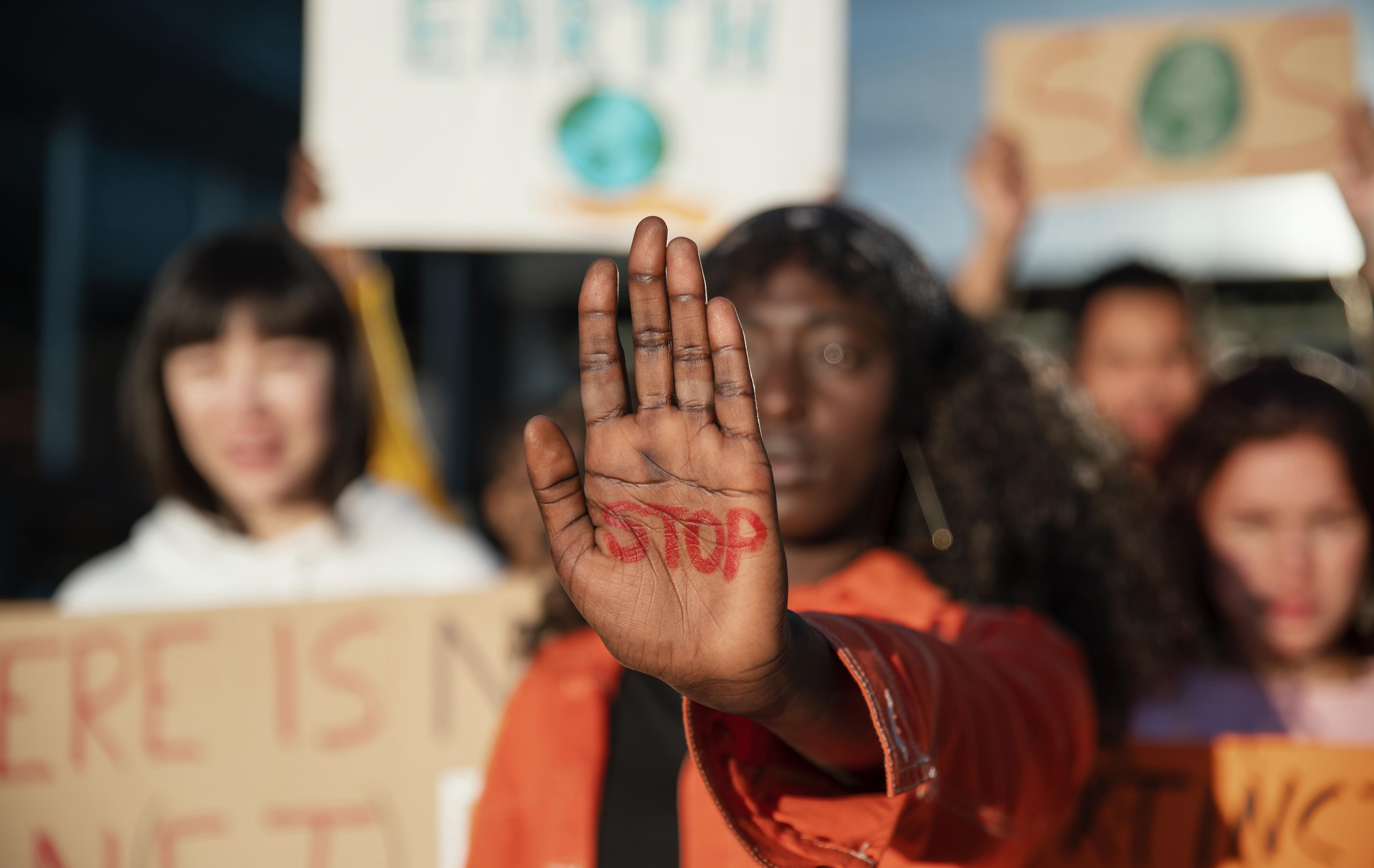 Mujer afrodescendiente al frente de una protesta climática muestra su mano con la palabra "STOP" escrita en rojo, en un acto de resistencia colectiva.