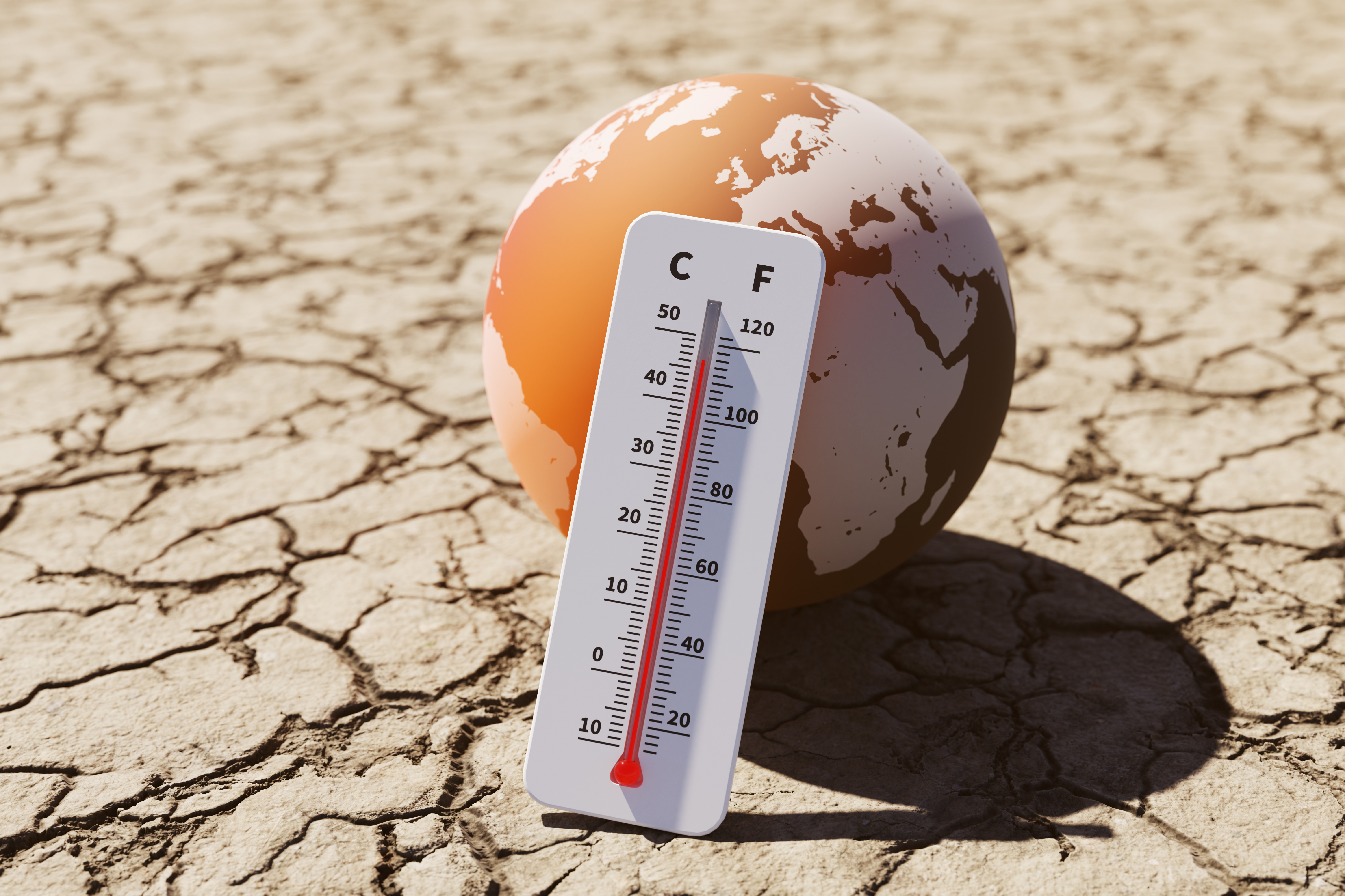 Termómetro con temperaturas elevadas frente a un globo terráqueo sobre suelo agrietado por sequía.