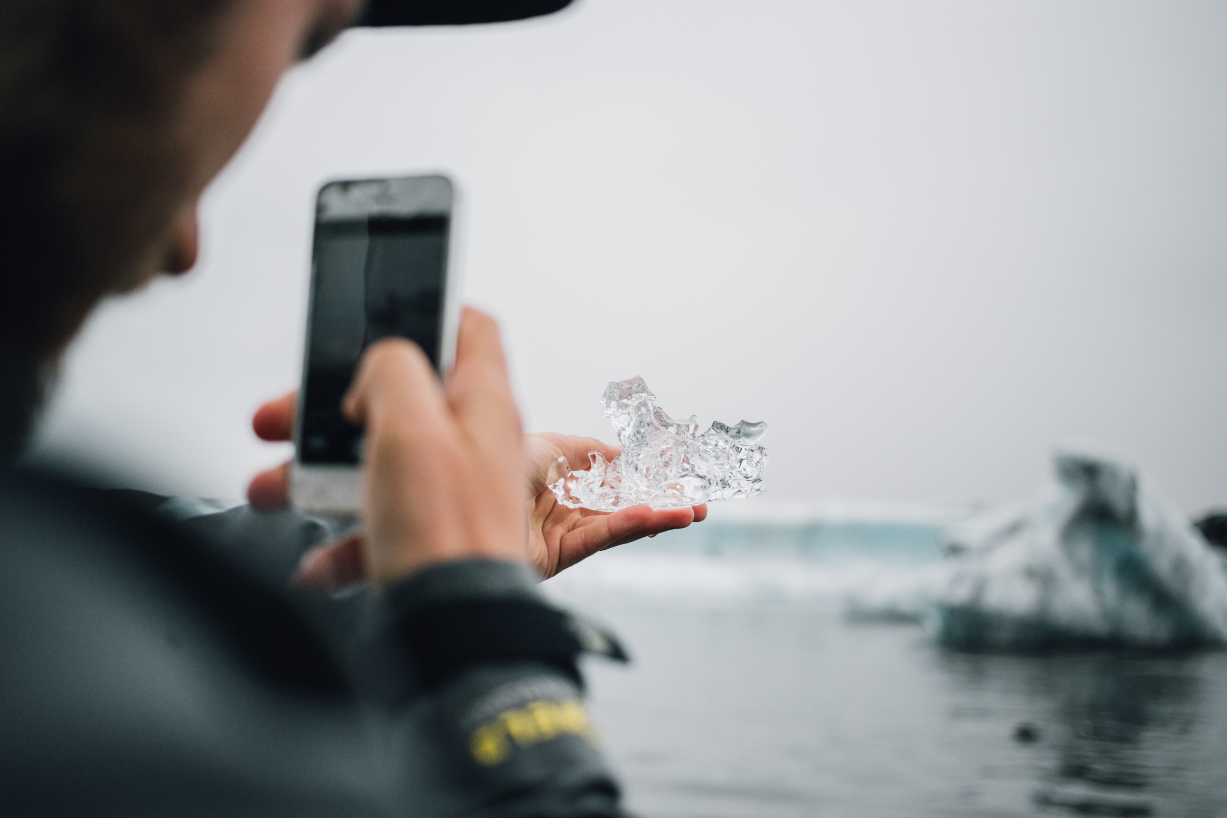 Persona fotografiando un trozo de hielo glaciar con su celular junto al mar en un paisaje polar.