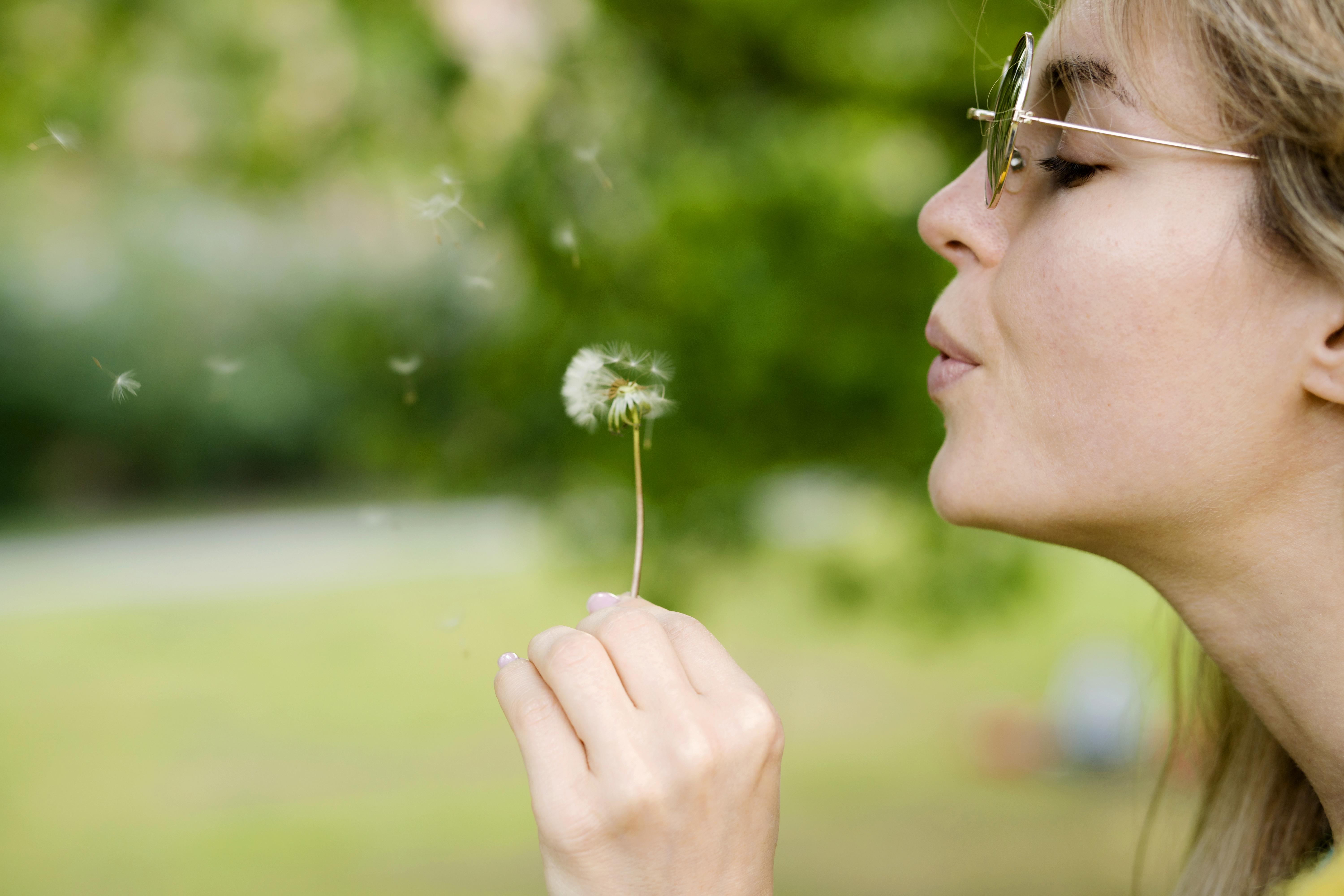 Mujer con gafas soplando un diente de león al aire libre.