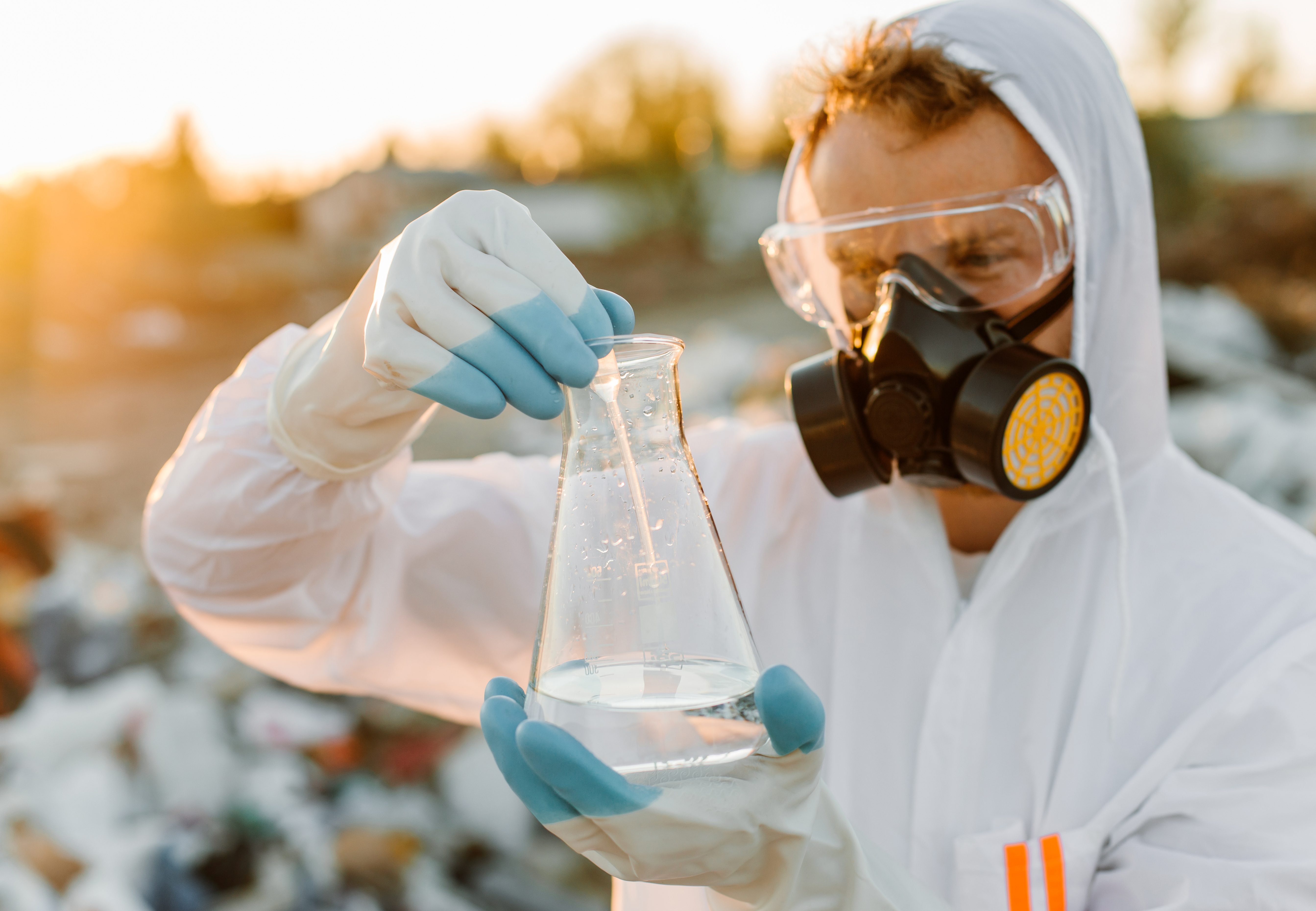 Investigador con traje protector y máscara antigás analiza agua contaminada en una zona afectada por residuos industriales.