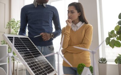Dos personas analizan un panel solar junto a modelos de turbinas eólicas en una oficina sostenible.