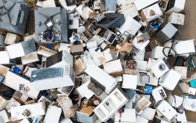 Vista aérea de un gran cúmulo de electrodomésticos y aparatos electrónicos desechados en un vertedero, con una persona entre ellos