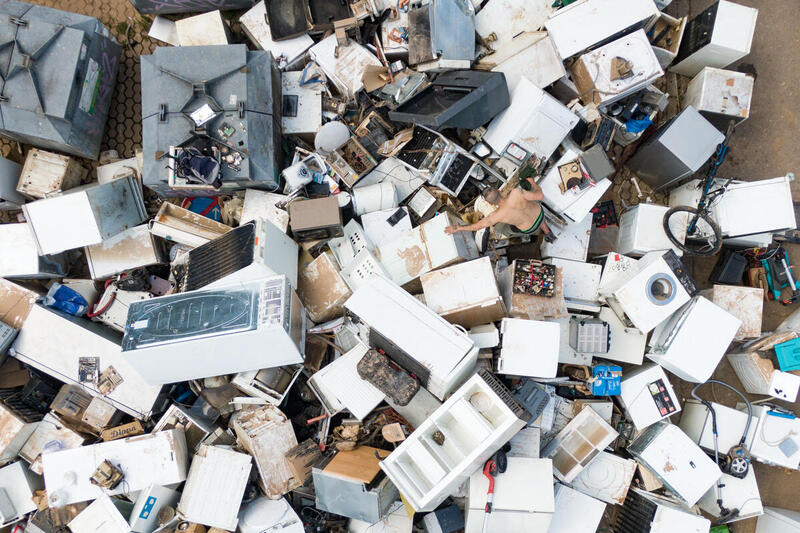 Vista aérea de un gran cúmulo de electrodomésticos y aparatos electrónicos desechados en un vertedero, con una persona entre ellos