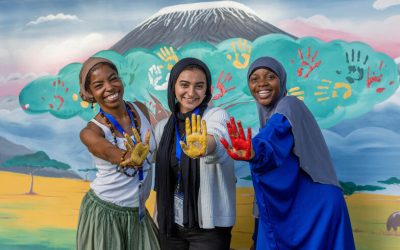 Tres mujeres jóvenes mostrando manos pintadas frente a un mural colorido