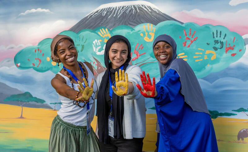 Tres mujeres jóvenes mostrando manos pintadas frente a un mural colorido