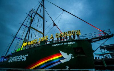Barco Rainbow Warrior de Greenpeace con luces que forman el mensaje "You Can’t Sink a Rainbow" en su cubierta durante la noche.