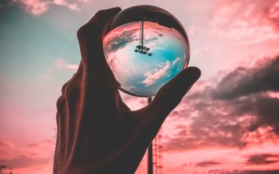 Mano sosteniendo esfera de cristal con reflejo invertido del cielo al atardecer