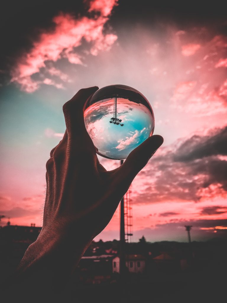 Mano sosteniendo esfera de cristal con reflejo invertido del cielo al atardecer