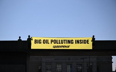 Activistas de Greenpeace despliegan una gran pancarta amarilla con el mensaje “BIG OIL POLLUTING INSIDE” frente a un edificio institucional, denunciando el impacto ambiental de las petroleras.