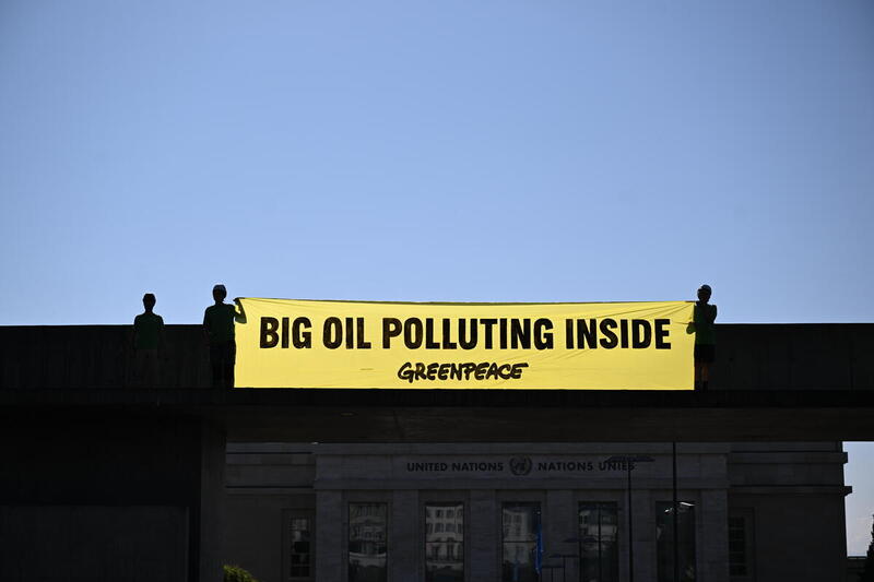Activistas de Greenpeace despliegan una gran pancarta amarilla con el mensaje “BIG OIL POLLUTING INSIDE” frente a un edificio institucional, denunciando el impacto ambiental de las petroleras.