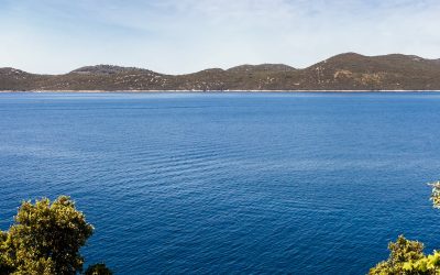 Vista panorámica de un lago azul profundo rodeado de colinas y vegetación verde bajo un cielo despejado con nubes ligeras.